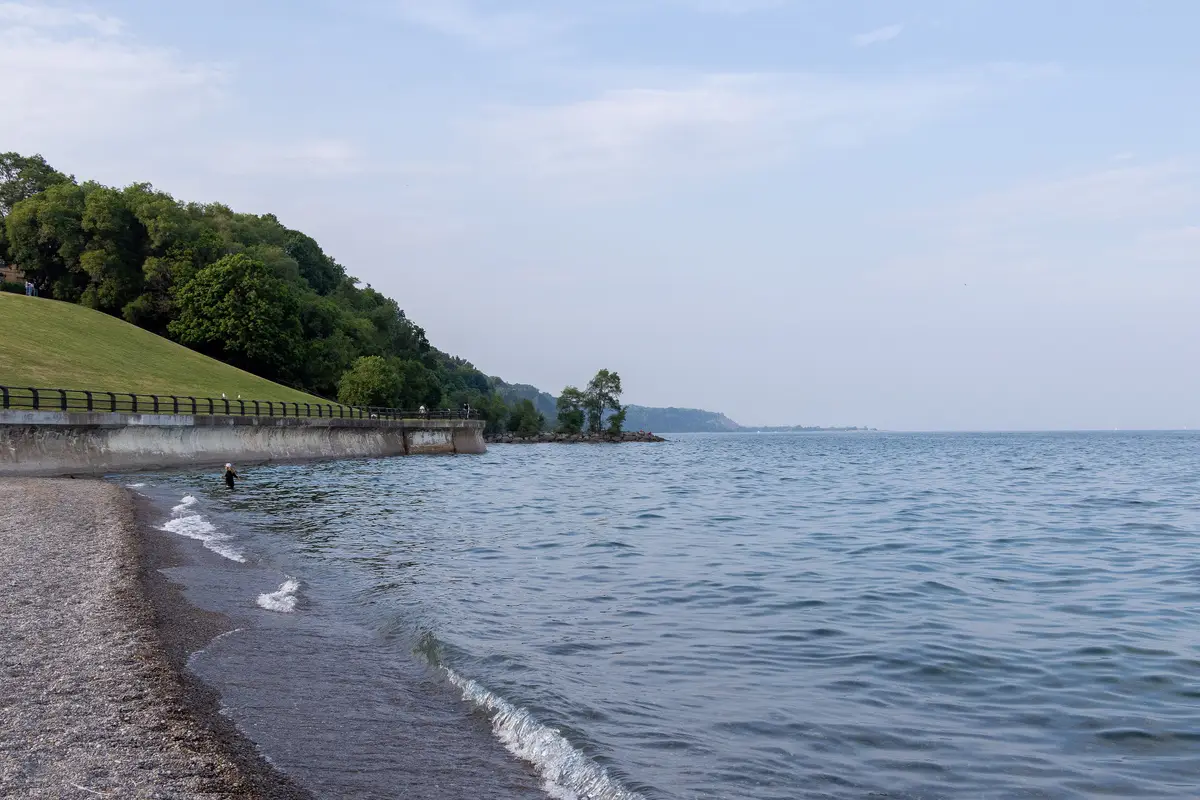 The Lake Ontario shoreline beside the plant grounds, with a stone wall, a grassy bank and the open lake beyond