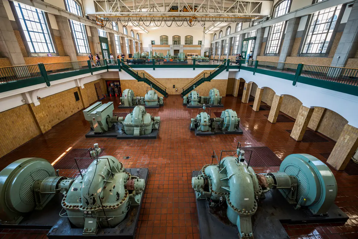 A large hall inside the plant, with green pump machinery on a tiled floor beneath tall windows and a railed gallery