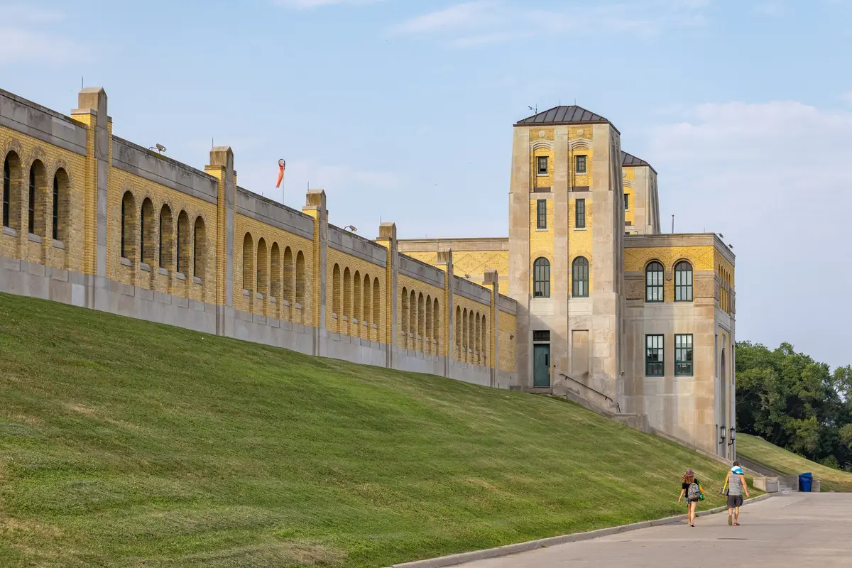 Yellow-brick facade and tall arched windows of the plant, with towers at each end and a grassy embankment below