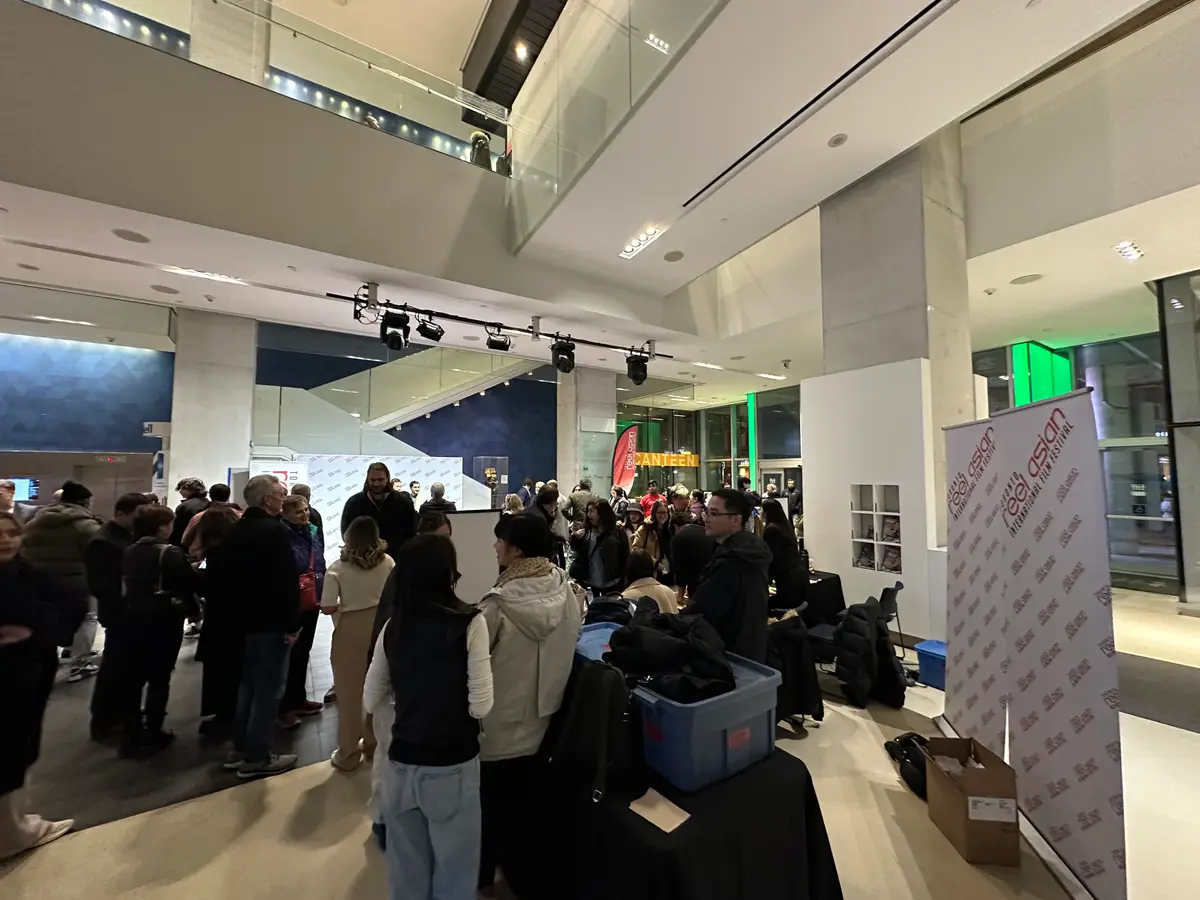 A crowd gathered in the open lobby of TIFF Bell Lightbox beside a step-and-repeat backdrop, with a balcony and track lights above.
