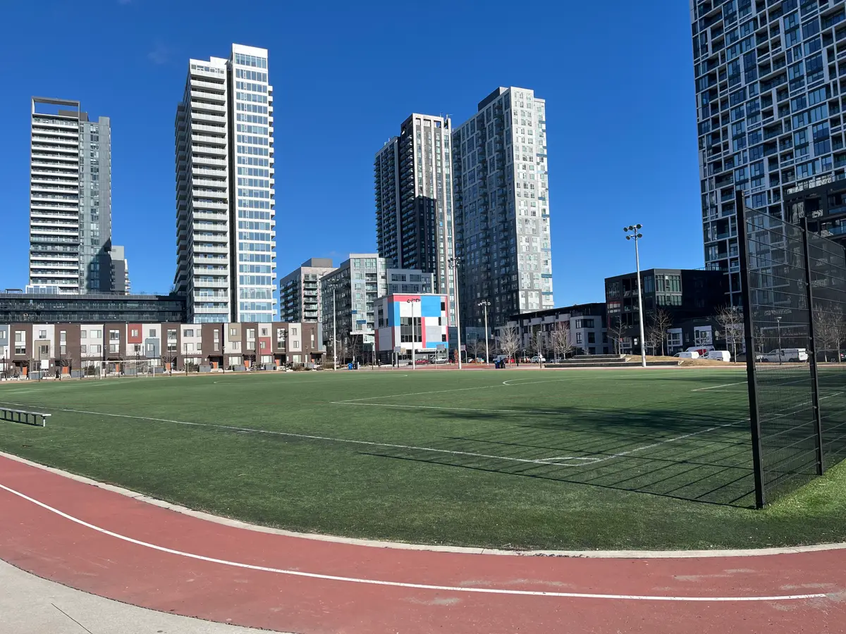 A turf field with a red running track around it, with residential towers behind