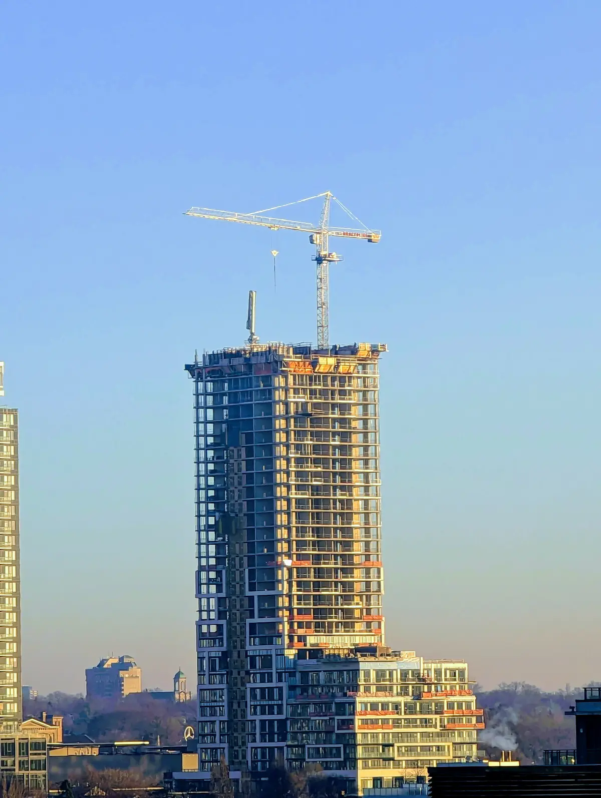 A tall tower under construction with a crane on its roof, against a clear sky