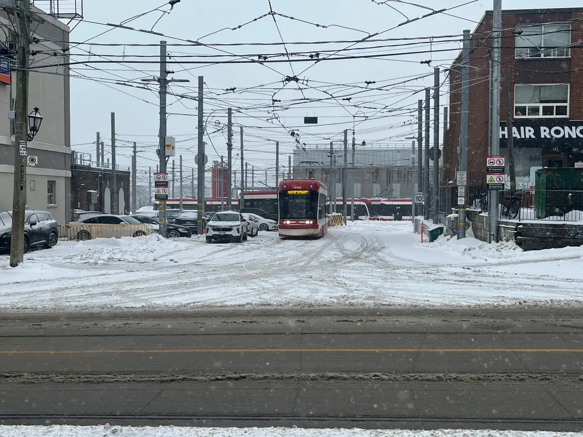 A red TTC streetcar crossing a snowy yard under a web of overhead wires at the Roncesvalles Car House