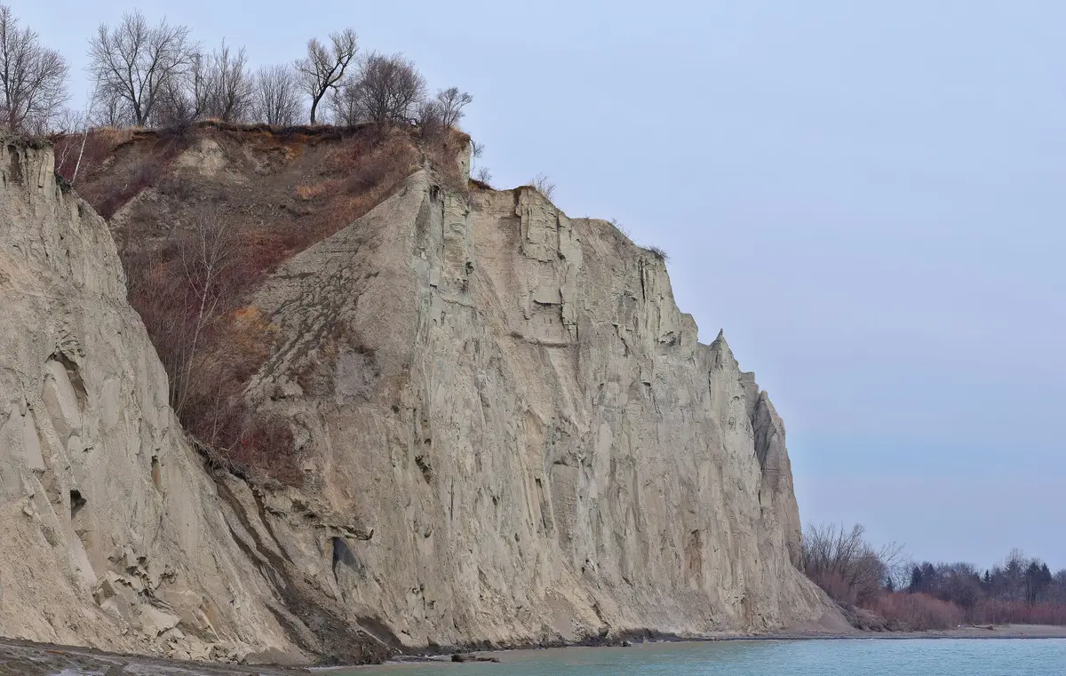Pale clay cliffs of the Scarborough Bluffs rising above the Lake Ontario shore under a grey-blue sky.