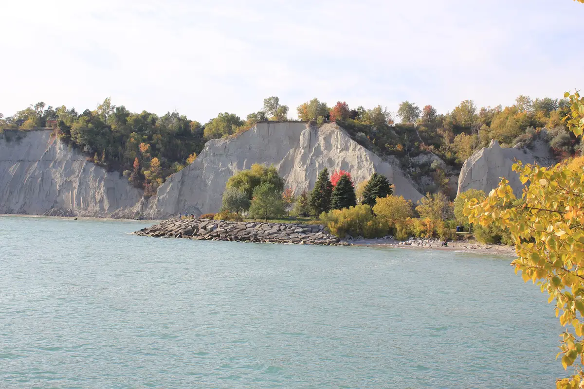 Autumn-coloured trees along the Scarborough Bluffs and a rocky point reaching into Lake Ontario.