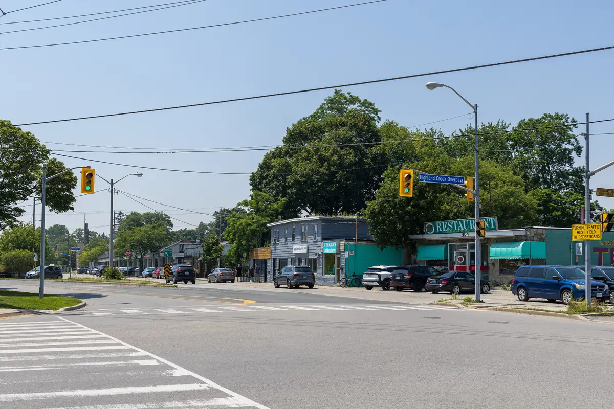 Looking west along Kingston Road in Highland Creek Village, with low storefronts, traffic lights and mature trees.