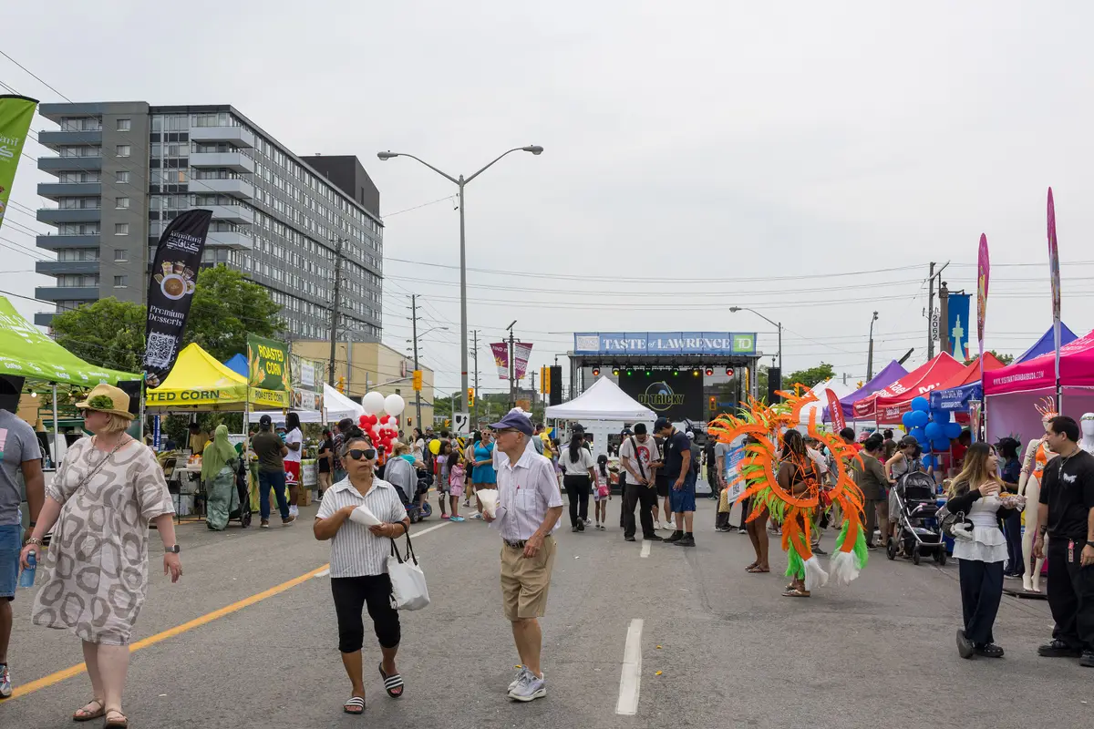 A closed stretch of Lawrence Avenue East filled with festival tents, a stage in the distance and people strolling.