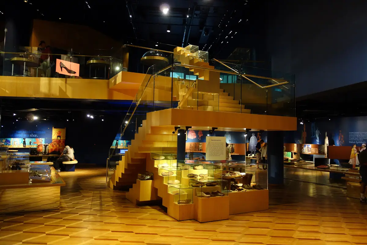 A dimly lit museum gallery with a golden stepped display structure and glass cases of footwear.