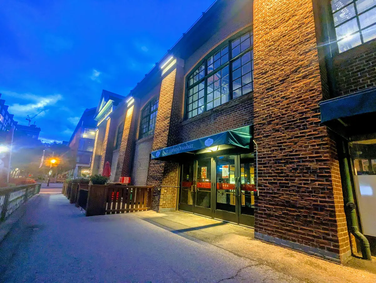 A St. Lawrence Market entrance under a green awning, lit up in the blue light of dusk