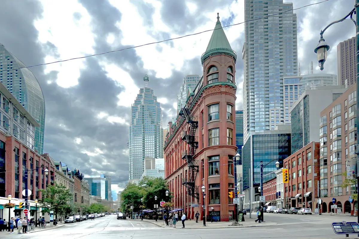 The Gooderham Flatiron Building's red brick wedge with downtown towers behind under a cloudy sky