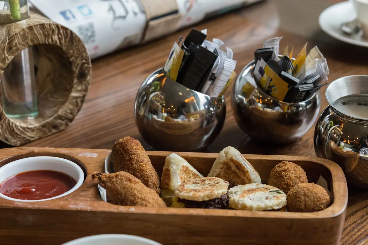 A wooden tray of Sri Lankan snacks: pol roti, egg rolls, vegetable roti and fish cutlets, with a small dish of sauce.