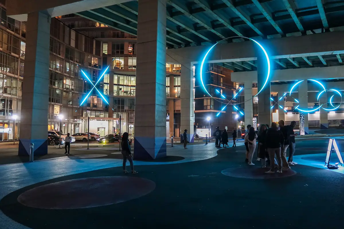 Blue glowing X and ring shapes under the Gardiner, with people standing nearby at night