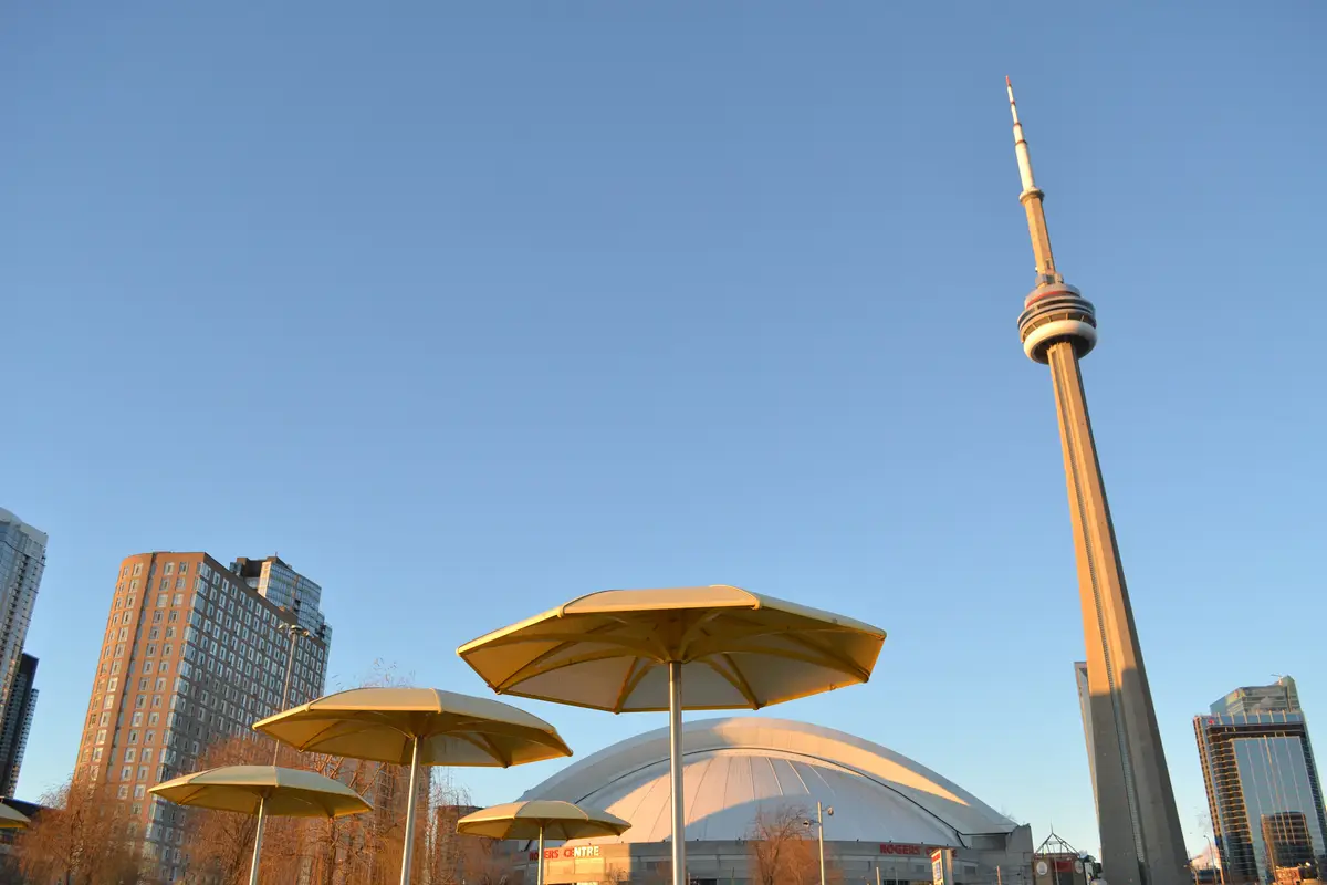 Round beige umbrellas at HTO Park with the CN Tower and condo towers against a clear sky