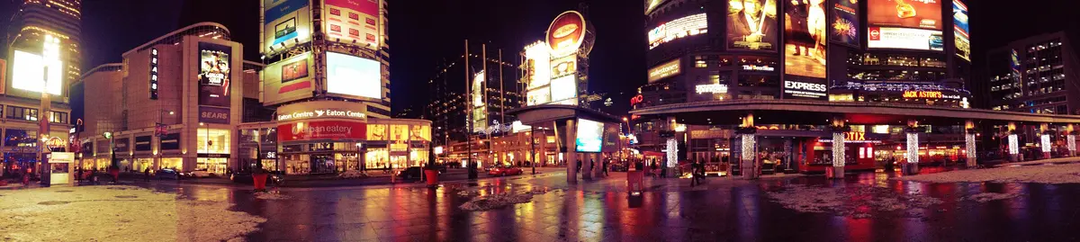 Yonge-Dundas Square at night, with lit billboards, wet pavement and patches of snow along the edges