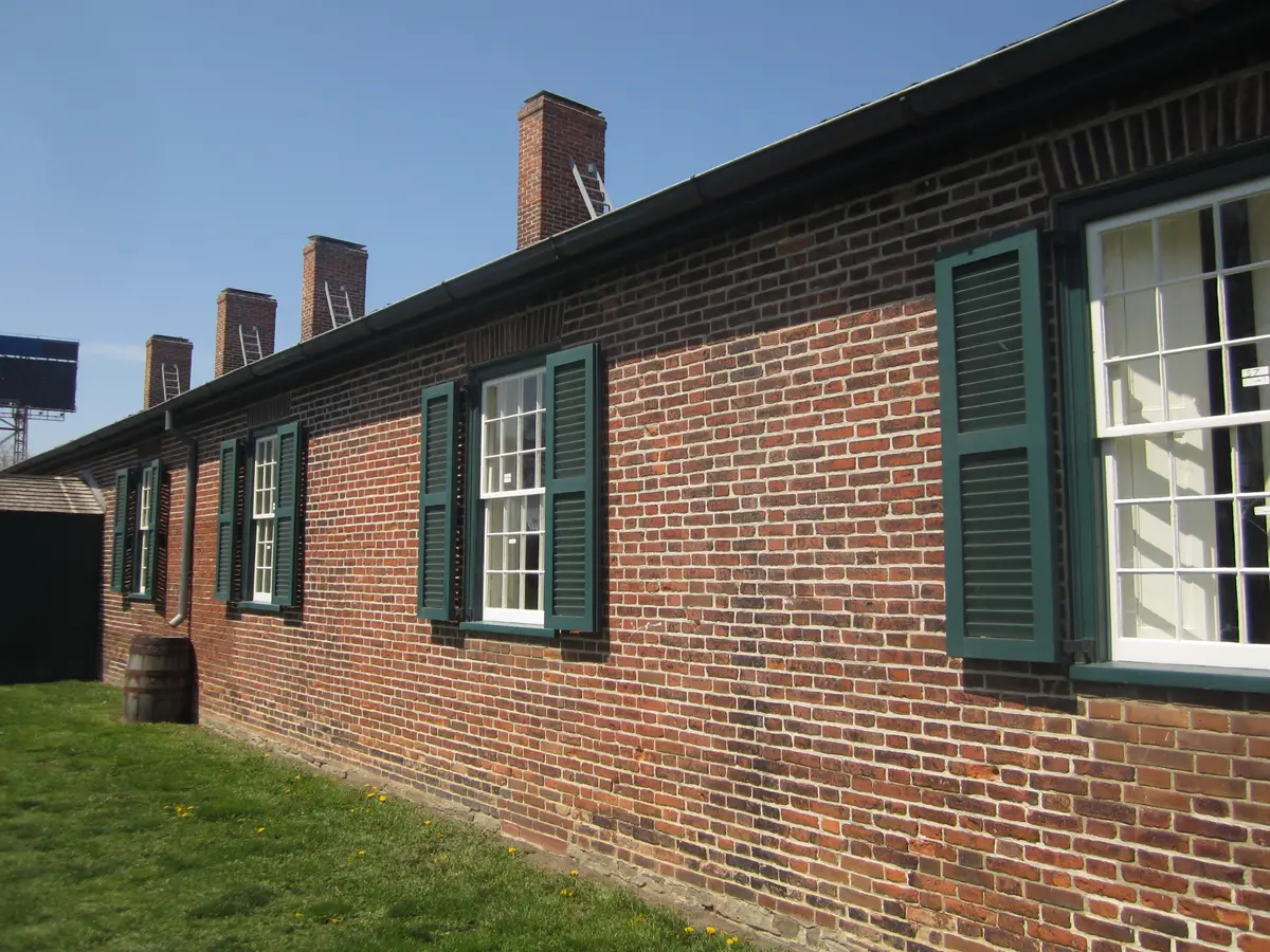 A long red-brick building with green shutters and tall chimneys on the lawn at Fort York