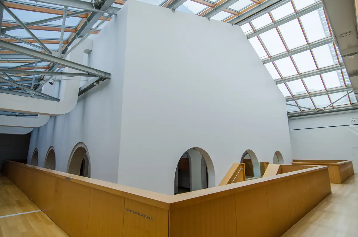A white gallery volume with arched openings under a glass and timber skylight