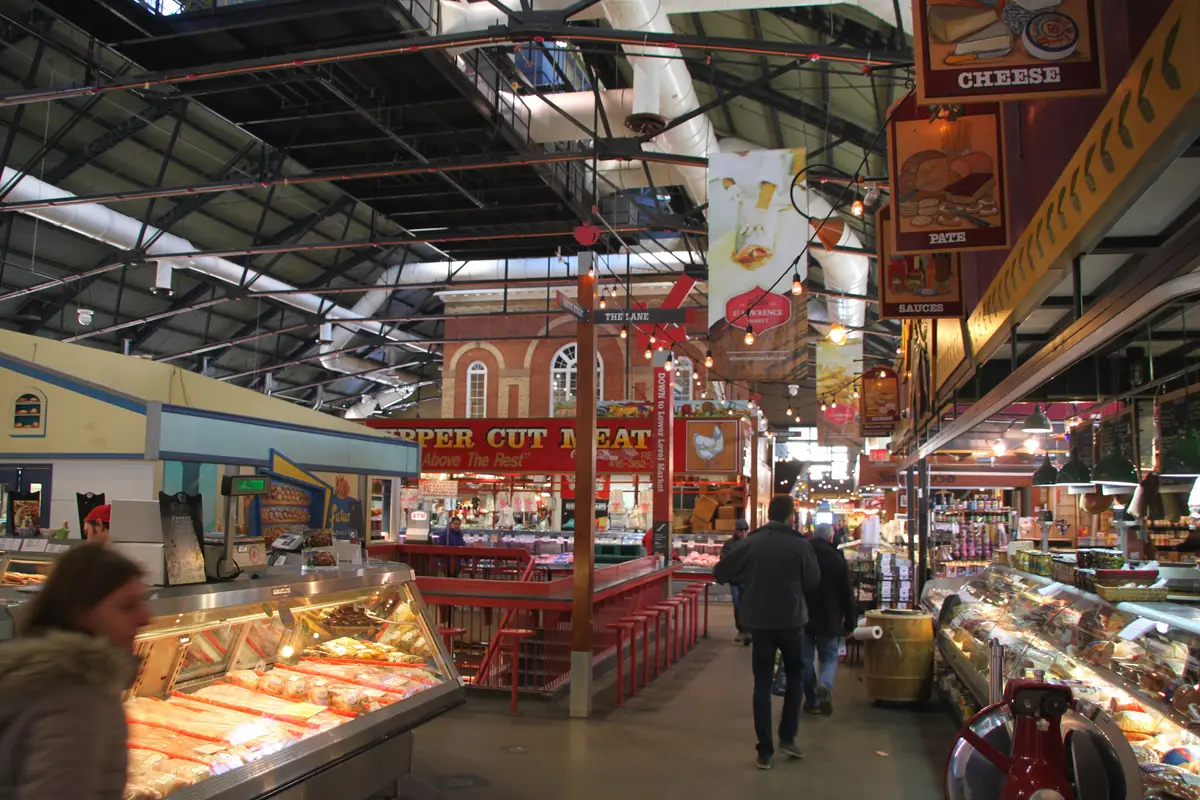 Shoppers walking between food counters under the arched steel roof of St. Lawrence Market