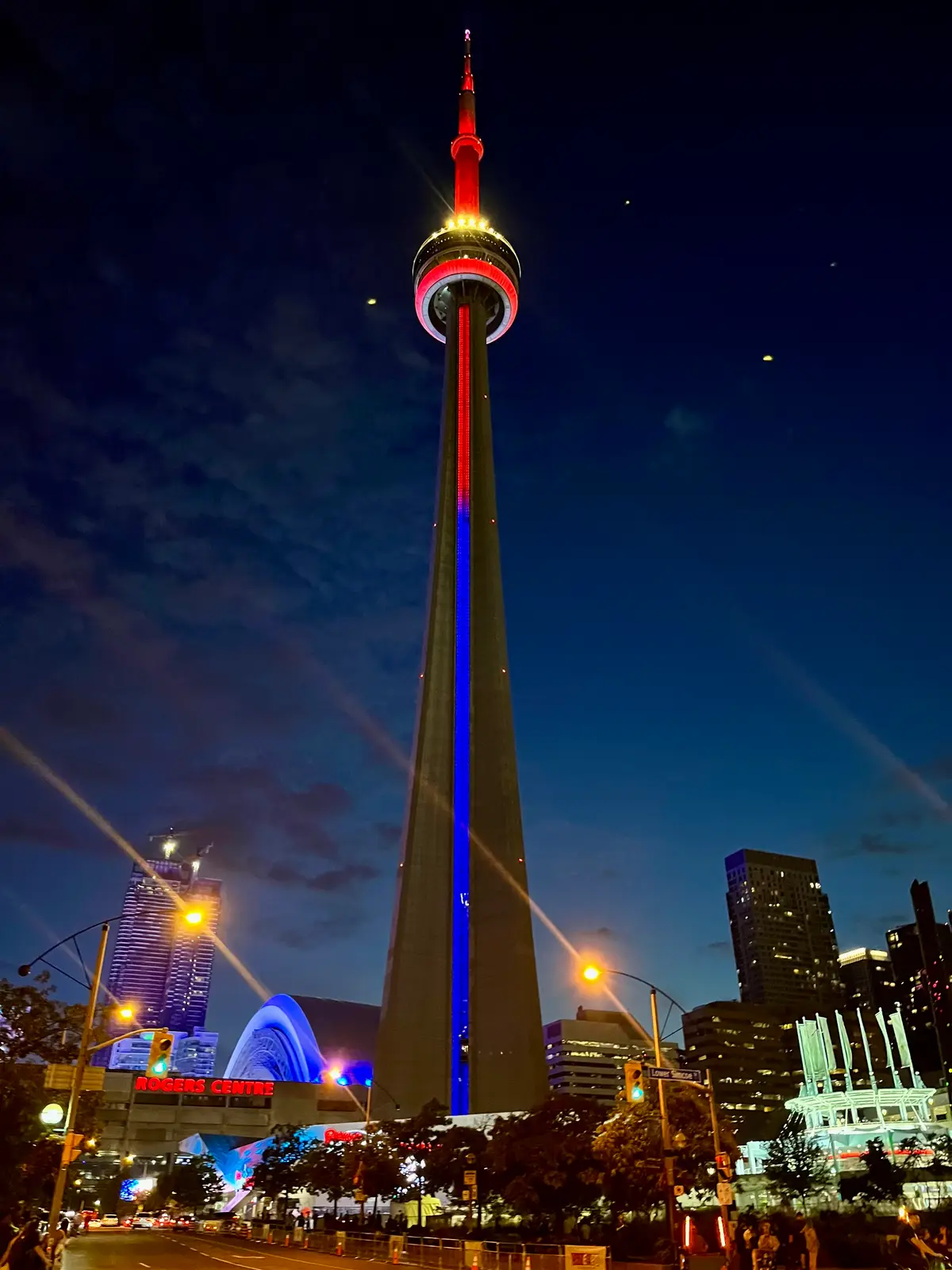 The CN Tower glowing red and blue against a dark night sky, seen from its base