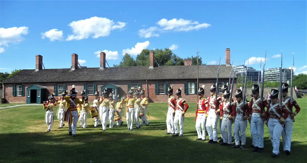 People in period uniforms standing in formation on the lawn in front of a long brick building