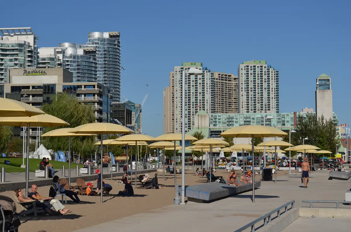 People relaxing in lounge chairs under yellow umbrellas on the HTO Park beach with condo towers behind