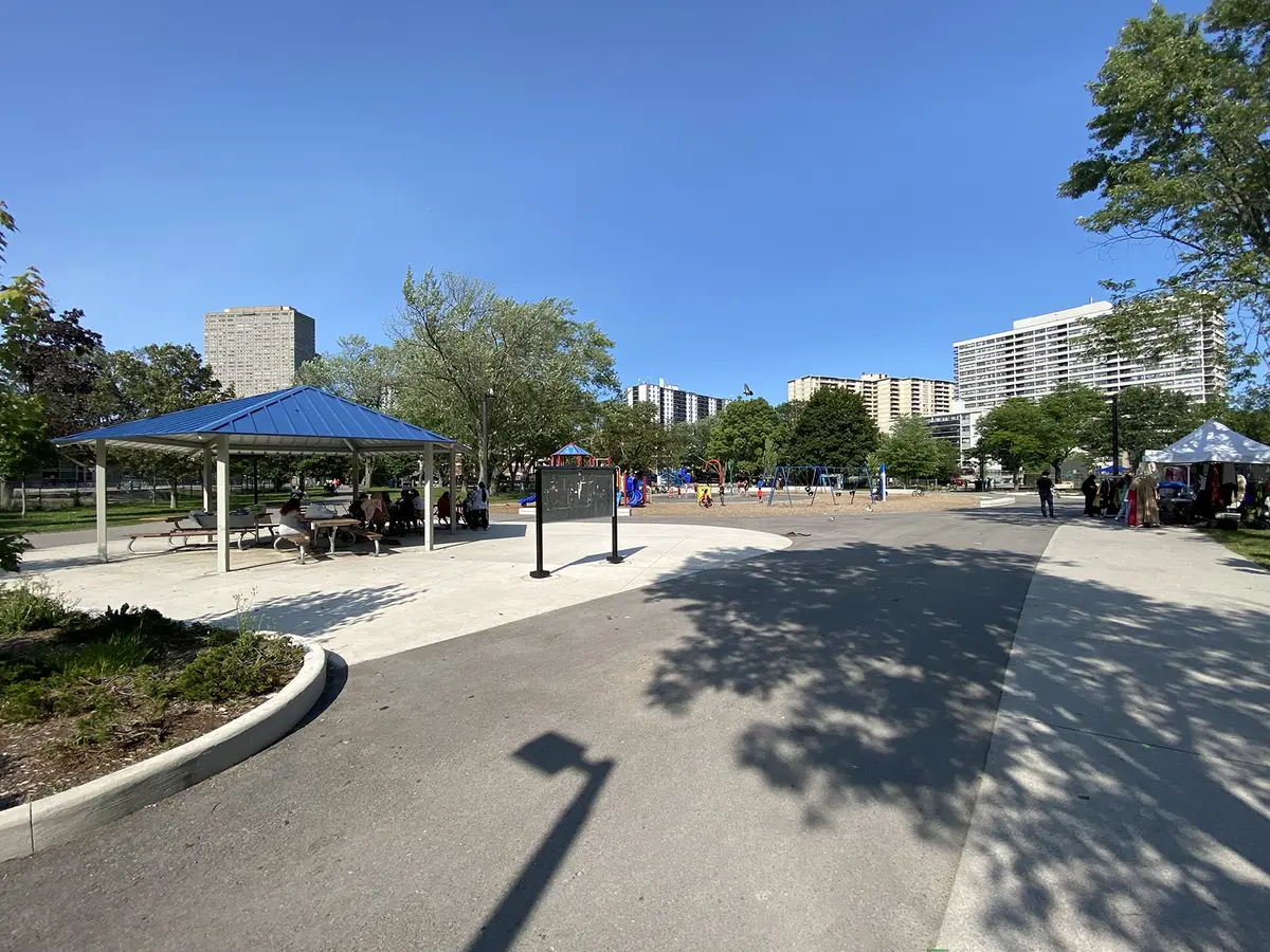 R.V. Burgess Park on a sunny day, with a blue-roofed shelter, a playground in the distance and a white tent at the right