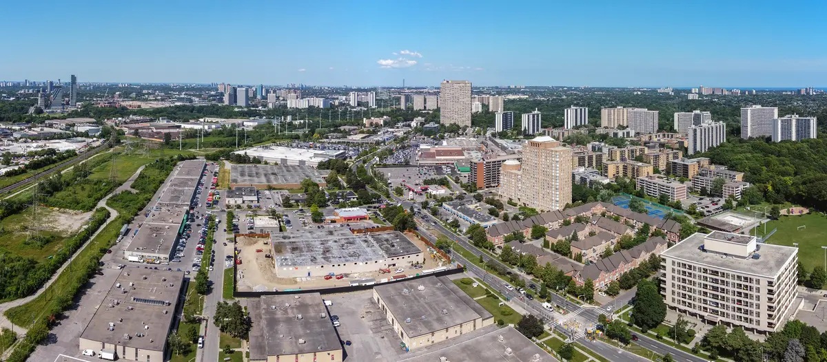 Aerial view of Thorncliffe Park: apartment towers, townhouse rows and low-rise commercial buildings under a clear blue sky