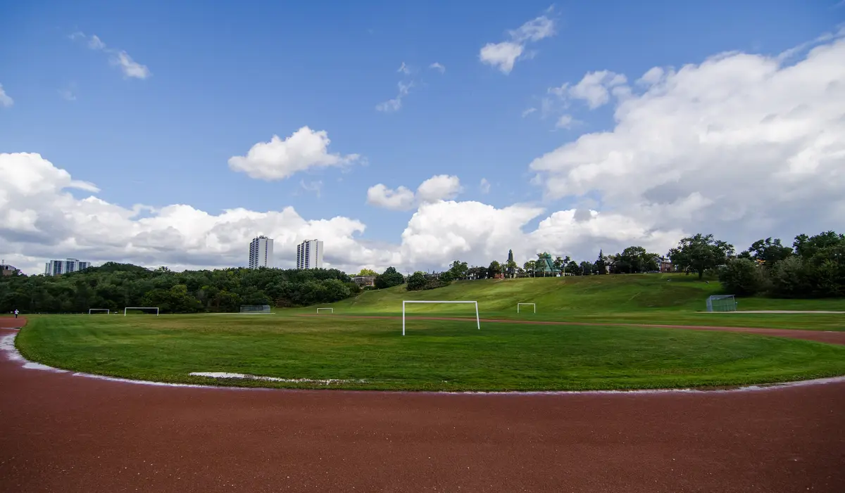 A grass sports field with white goal posts and a red running track, with towers in the distance