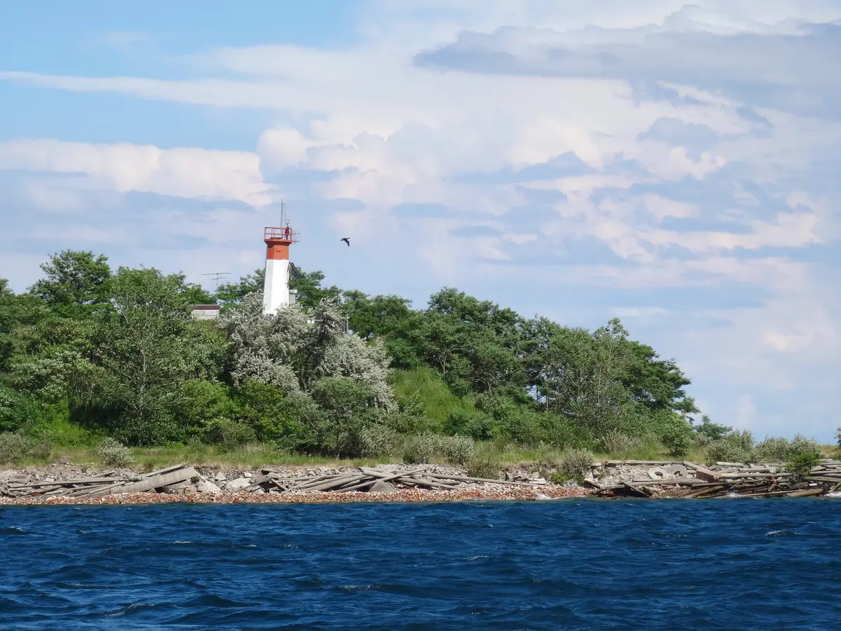 A small white lighthouse with a red top on a wooded point, with blue lake water in front.