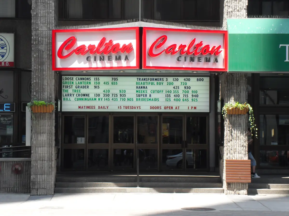 The entrance of Carlton Cinema, with two red illuminated Carlton Cinema signs above a letterboard of film titles