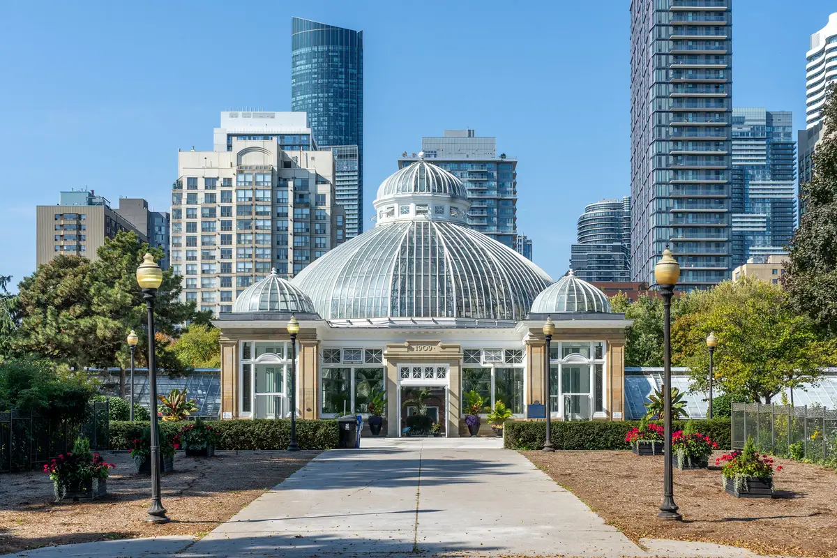Glass-domed pavilion of Allan Gardens Conservatory under a clear blue sky, with apartment towers rising behind