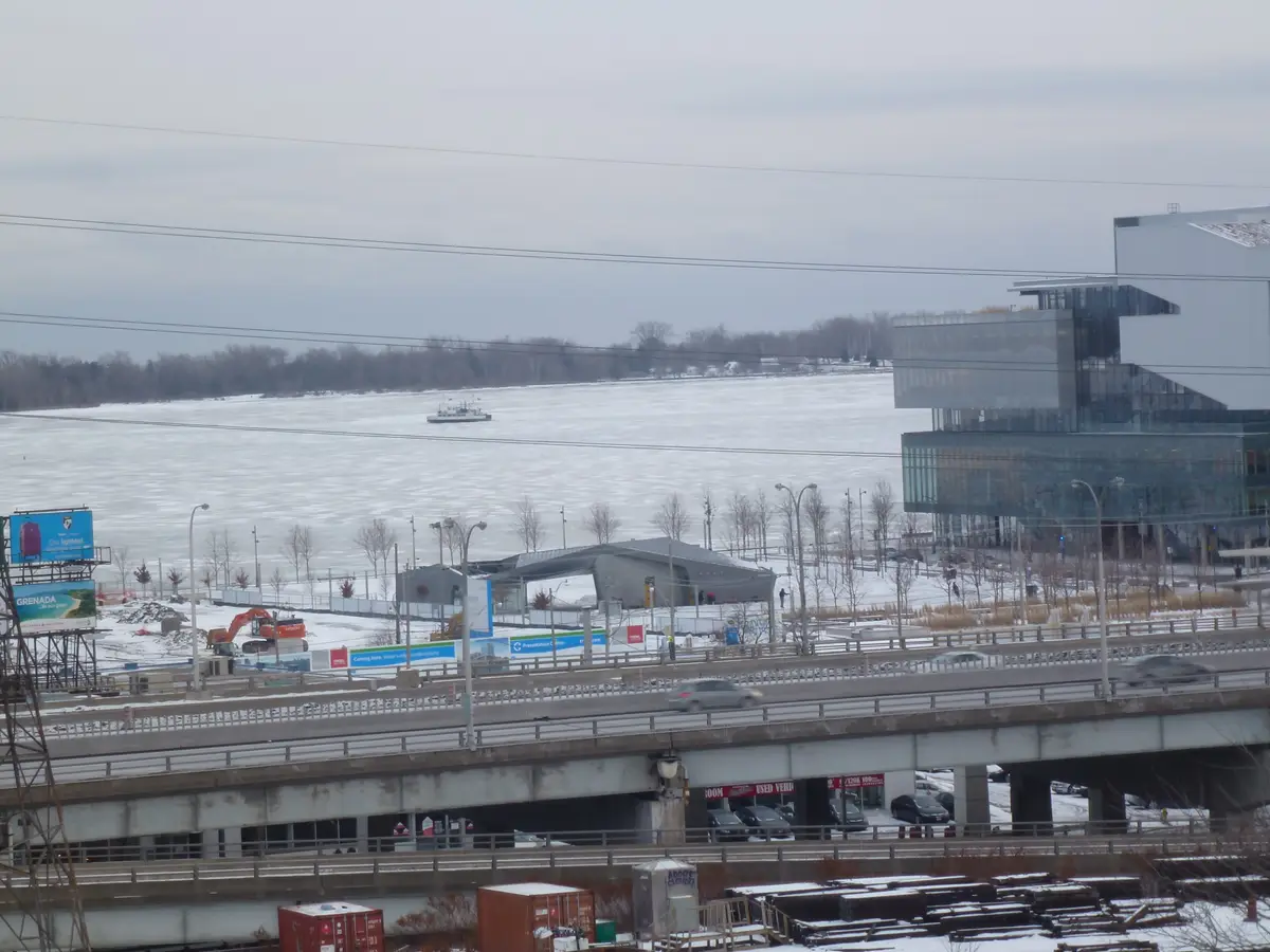 Ice and snow covering Toronto harbour, with the lakeshore, a highway and the waterfront buildings beyond.