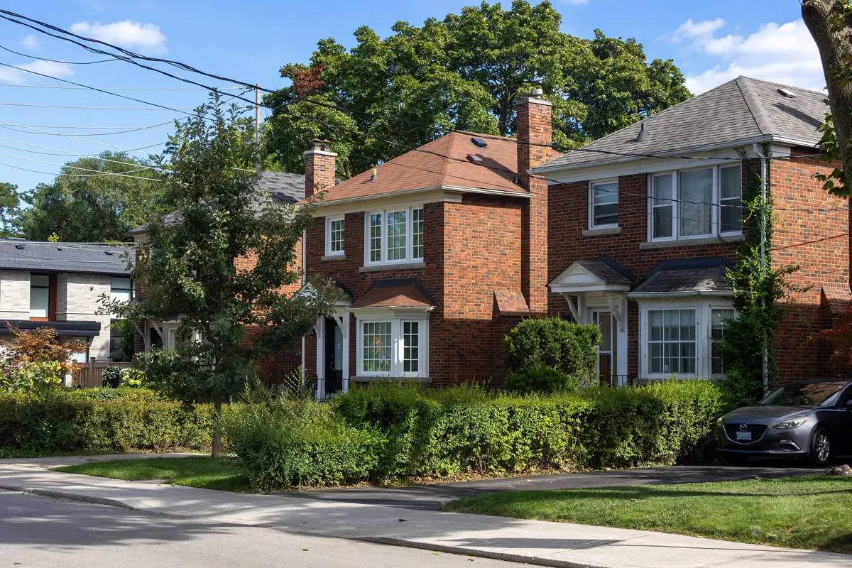 Brick houses with steep roofs behind leafy front yards on a quiet residential street.