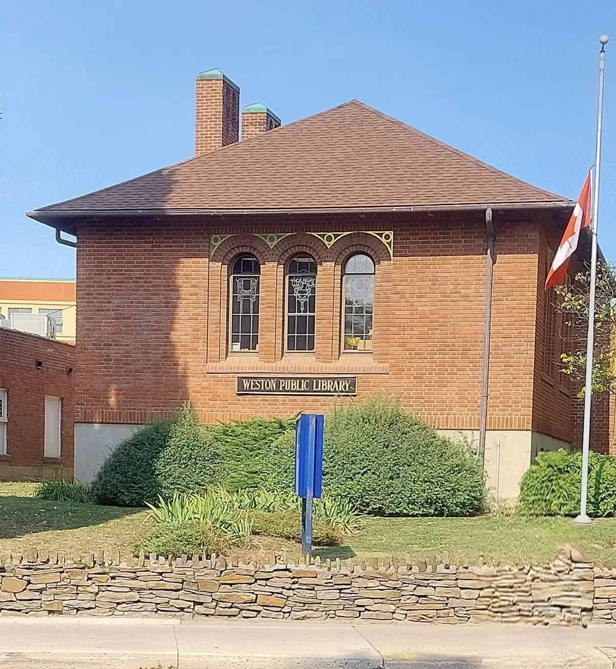 Brick wall of the Weston branch with three arched windows of patterned glass and a sign reading Weston Public Library