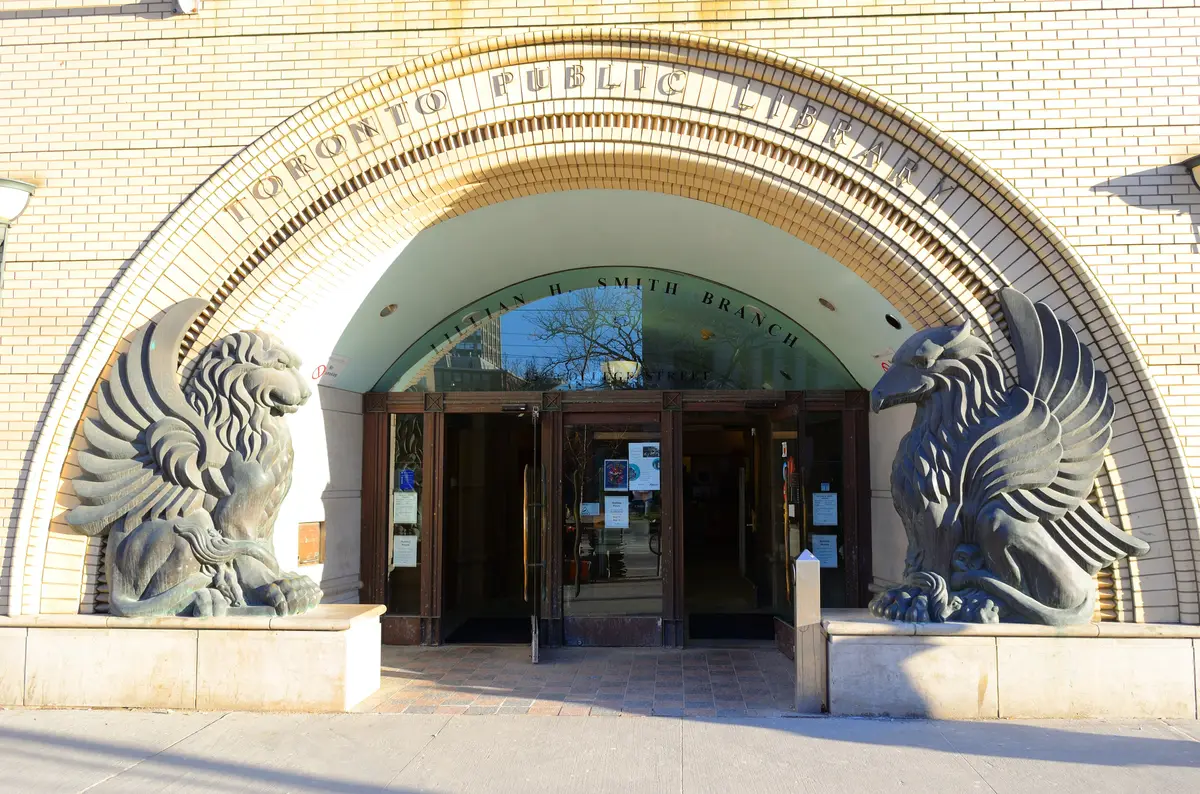 Entrance of the Lillian H. Smith branch, with two large sculpted winged figures flanking the doors and Toronto Public Library carved in the arch above