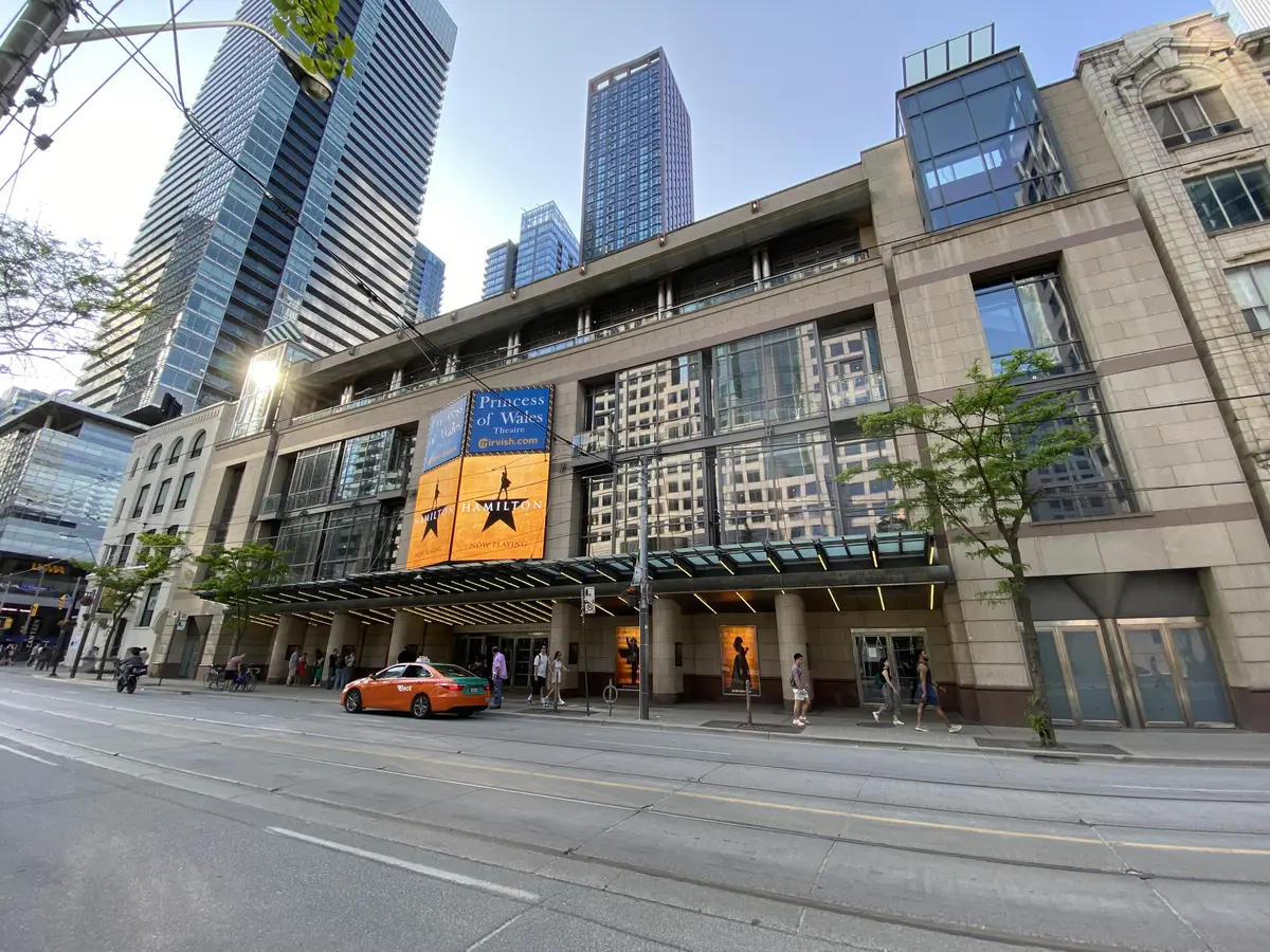 Front of the Princess of Wales Theatre, with a large Hamilton banner above the entrance and pedestrians on the sidewalk.