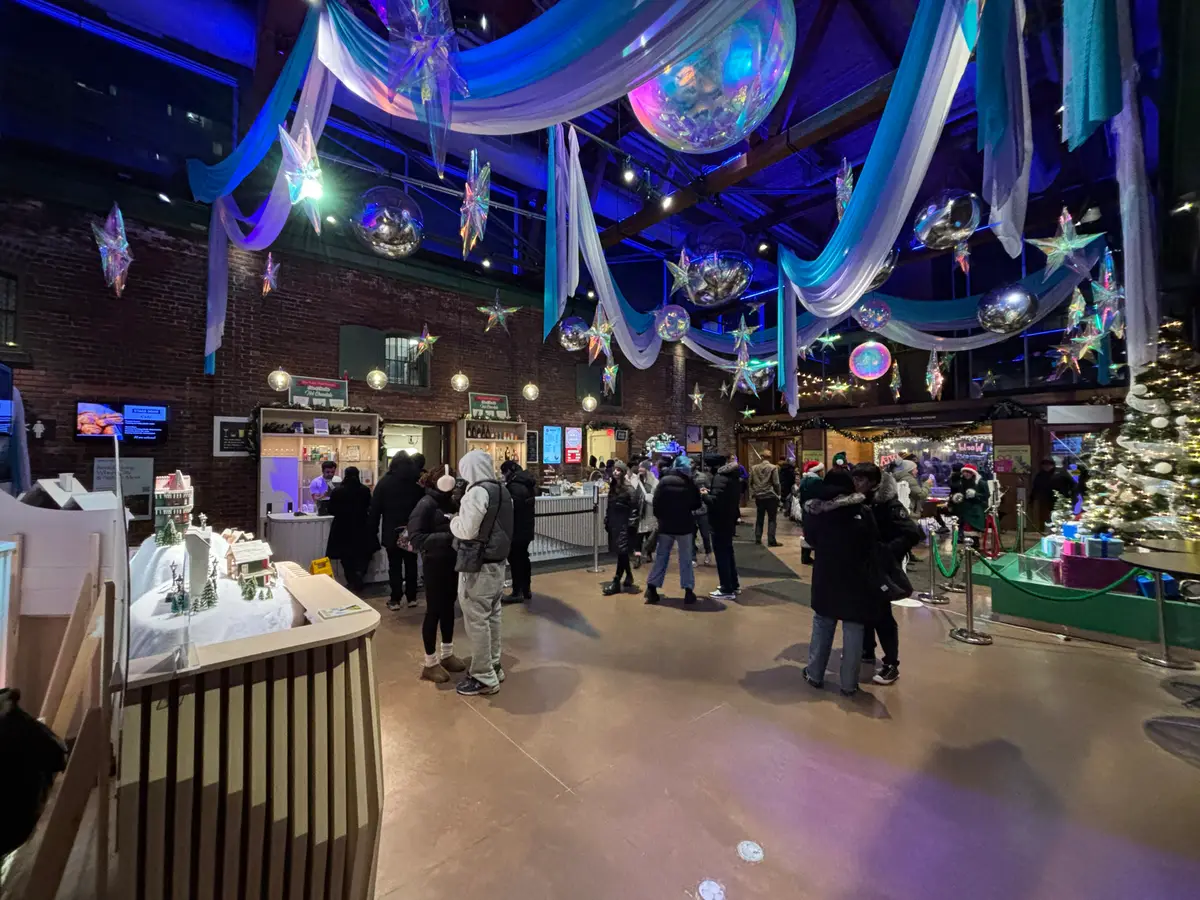 Lobby of the Young Centre with blue and silver holiday decorations, a Christmas tree and visitors under a brick wall.