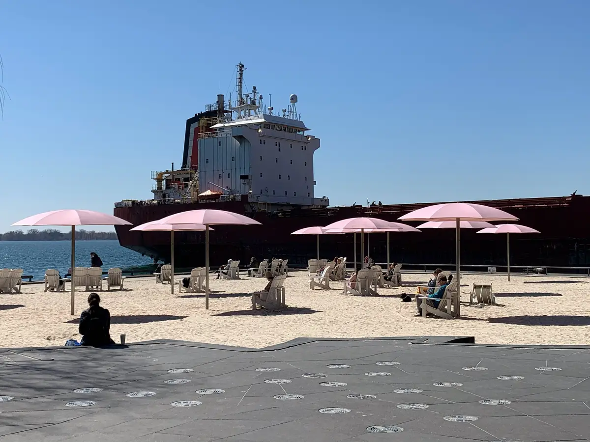 Pink umbrellas and lounge chairs on the sand at Sugar Beach, with a large ship in the background.