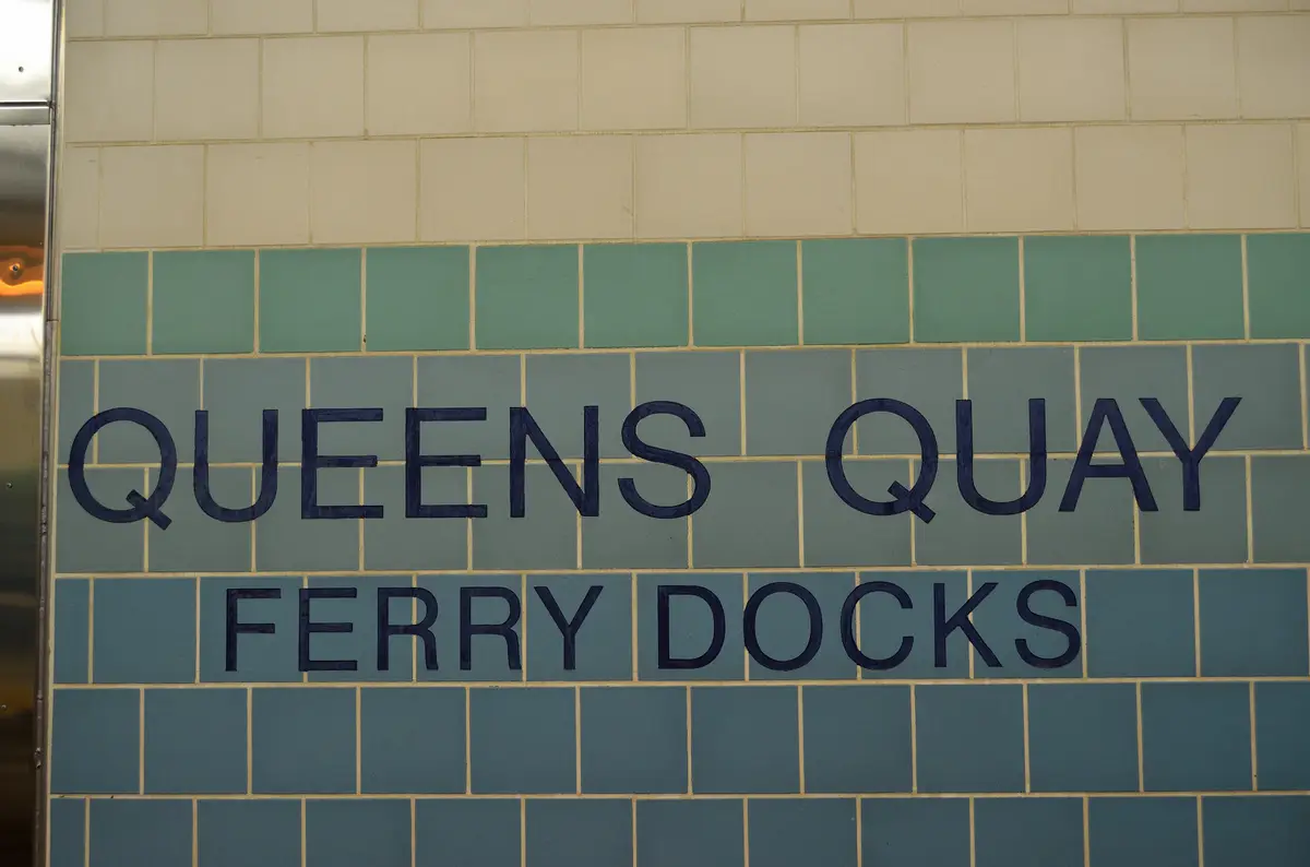 Cream and blue-green tiled station wall with the words QUEENS QUAY and FERRY DOCKS lettered in dark blue
