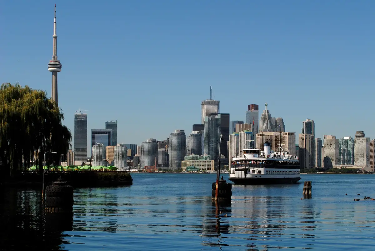 A white Toronto Island ferry crosses the harbour toward the downtown towers, with the CN Tower rising on the left