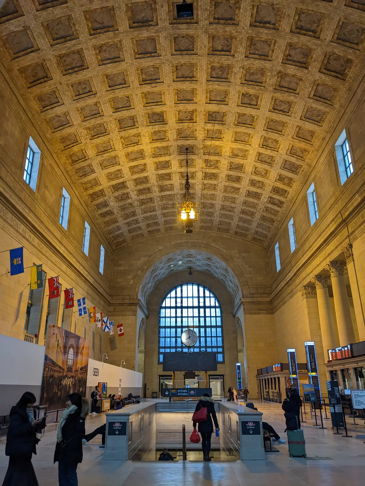 Inside Union Station's Great Hall, with a coffered ceiling, flags along one wall and an arched window at the far end