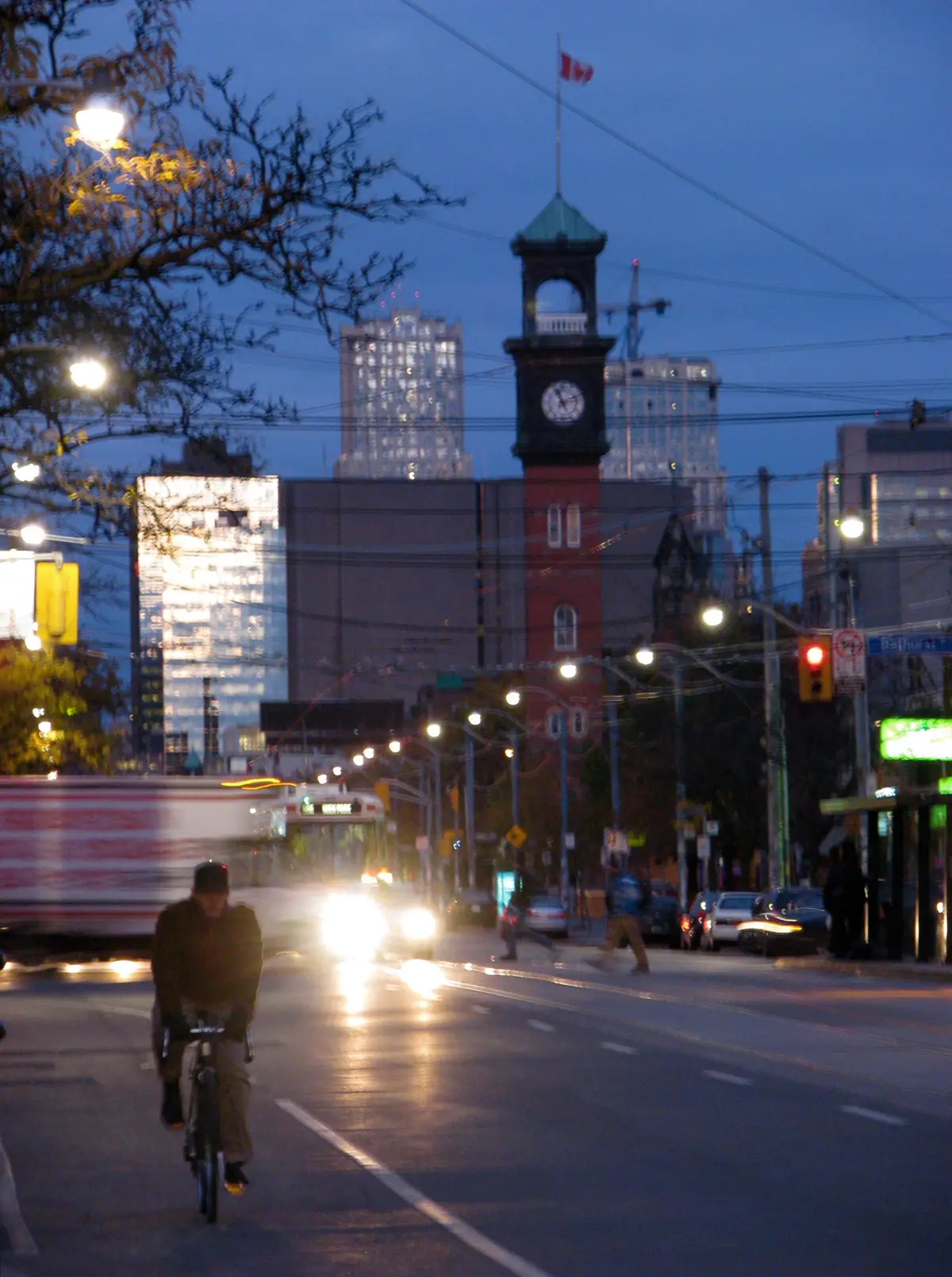 A cyclist on College Street at night, with a red-brick clock tower ahead