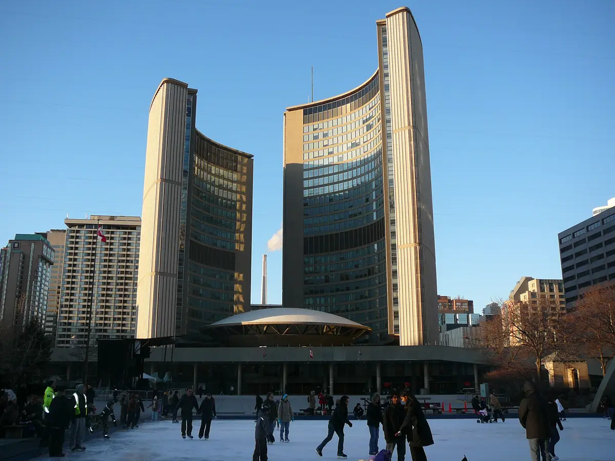 Skaters on the rink in front of Toronto City Hall's curved towers under a clear blue winter sky