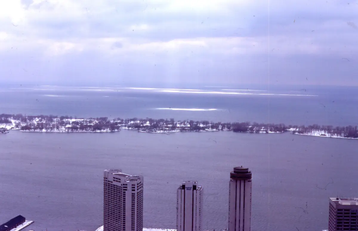 A snow-dusted strip of the Toronto Islands beside open lake water, seen from high above the downtown towers
