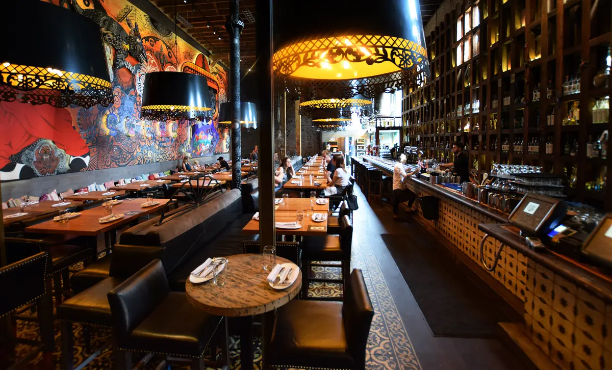 A Toronto restaurant dining room with set wooden tables, a long bar and a colourful mural, photographed in 2017