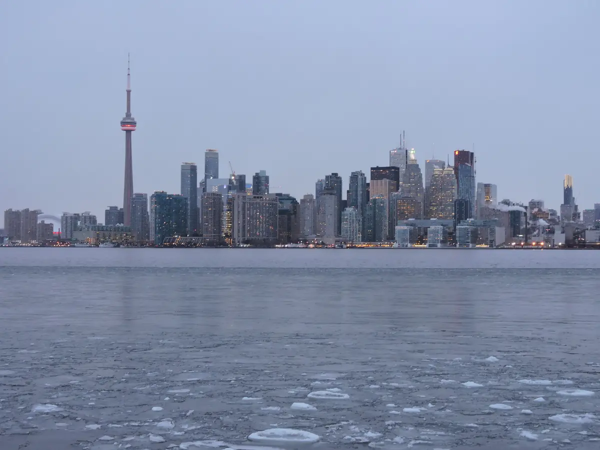 The Toronto skyline and CN Tower at dusk across the lake, with broken ice floating in the water in the foreground
