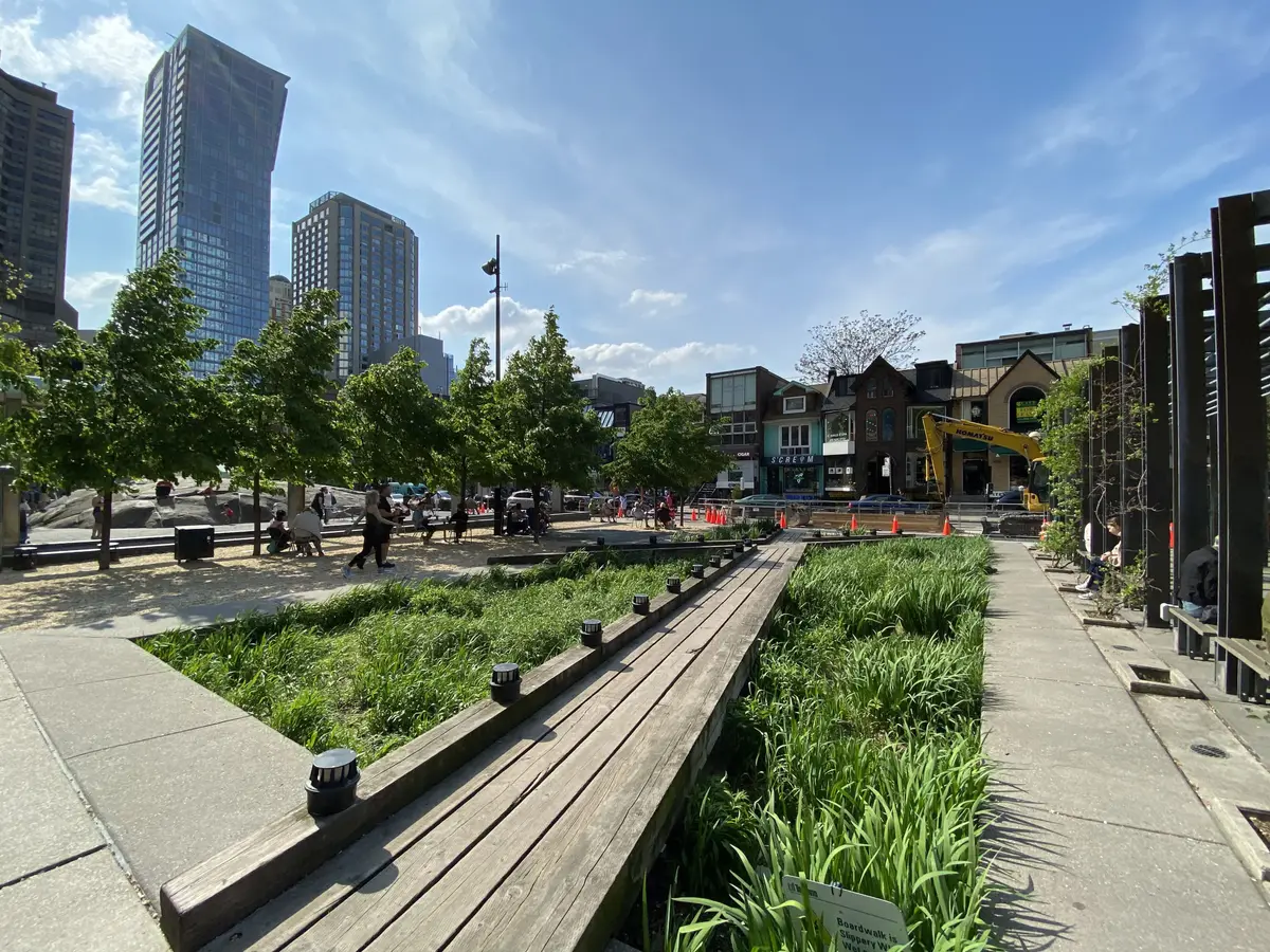Village of Yorkville Park with a raised wooden walkway, planted beds and towers behind